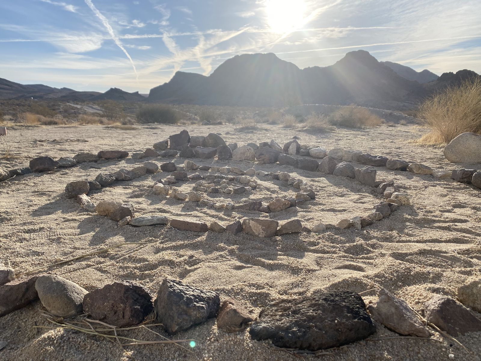 A stone labyrinth laid out on desert sand below rugged mountains